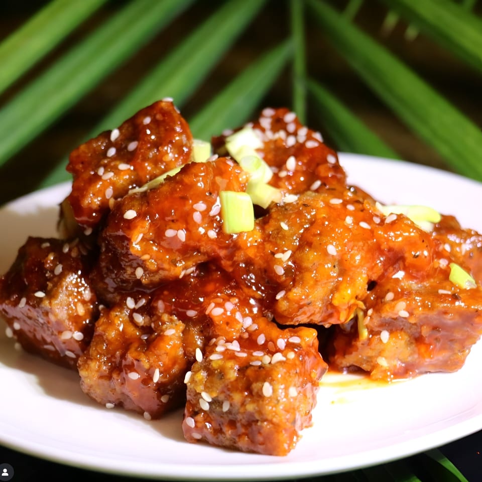 Vegan sweet and sour nuggets, garnished with sesame seeds and chopped green onions, on a white plate.