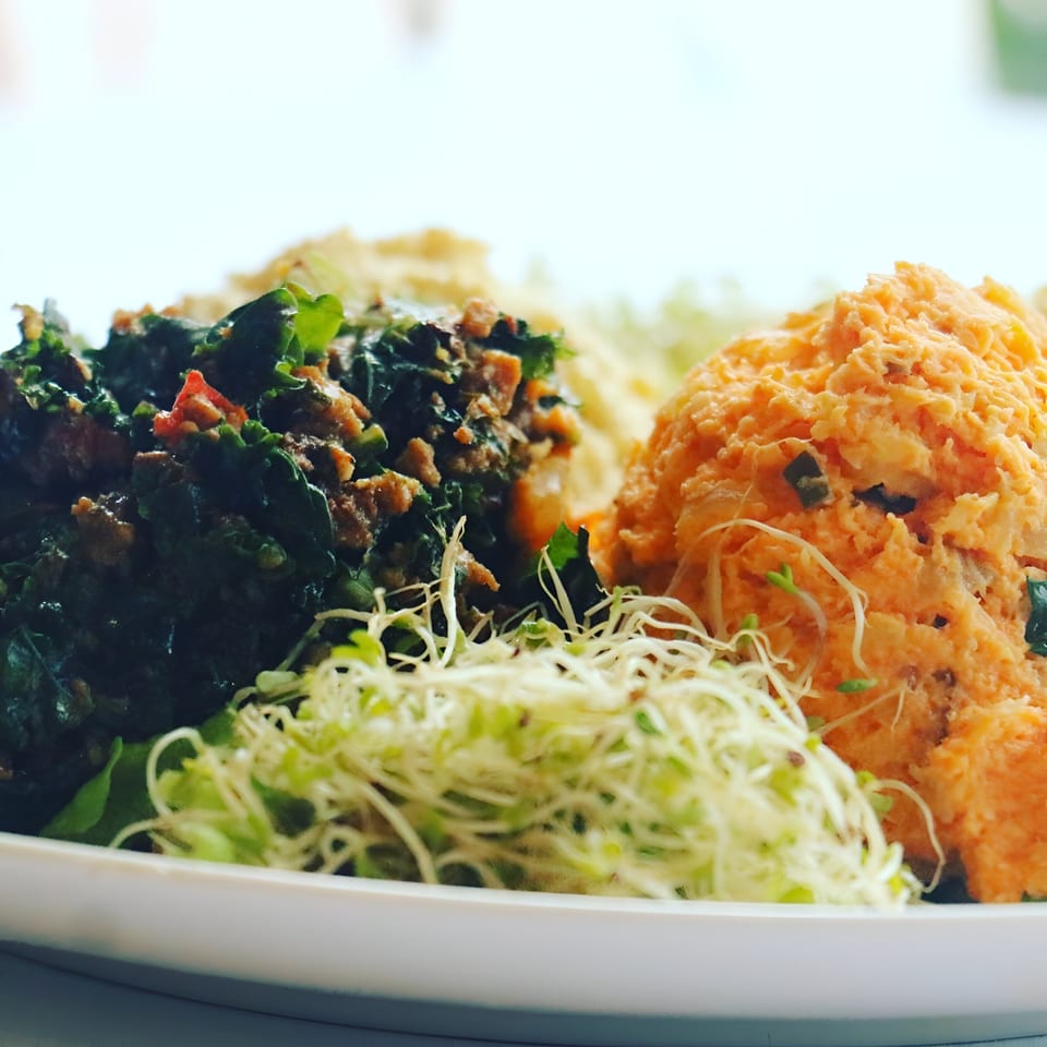 A vegan plate with dark green kale, orange mashed sweet potato, and light green sprouts.